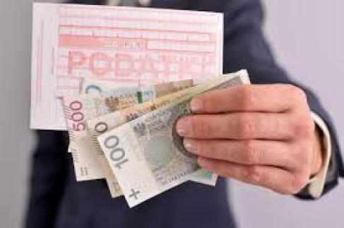 Ręka trzymająca blankiet przelewu z napisem podatki oraz banknoty o nominale sto, dwieście i pięćset złotych